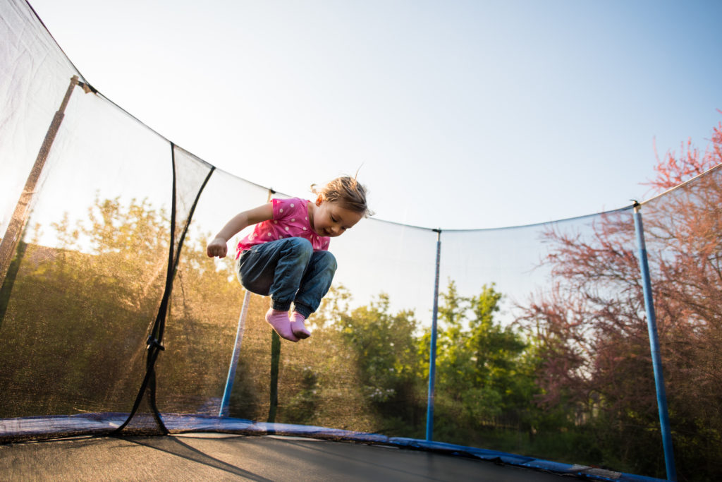 little girl jumping on trampoline in backyard